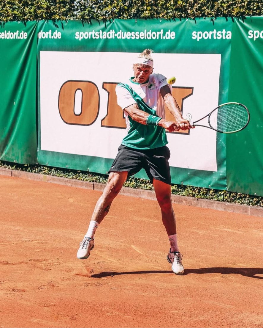 Robin Kern im Sprung beim beidhändigen Rückhandschlag auf Sand